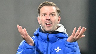 Fußballtrainer Florian Kohfeldt von Darmstadt 98 reckt am Spielfeldrand ungläubig die Arme hoch.