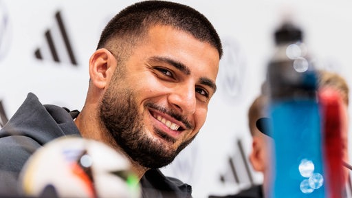 Der deutsche Nationalspieler Deniz Undav grinst schelmisch auf dem Podium einer Pressekonferenz während der EM.