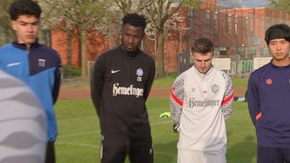 Fußball-Spieler der SV Hemelingen, Muhammed Sanneh und Abdula Genaev, stehen mit anderen Spielern bei einer Ansprache des Trainers auf dem Platz.