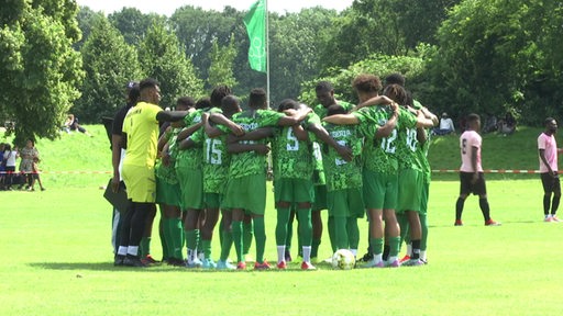 Dunkelhäutige Spieler einer Fussballmannschaft stehen in einem Kreis auf einem Fußballplatz