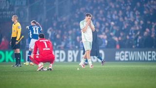 Werder-Spieler Senne Lynen schlägt bitter enttäuscht die Hände vors Gesicht nach dem Pokal-Aus in Bielefeld, neben ihm hockt Torwart Michael Zetterer auf dem Rasen.