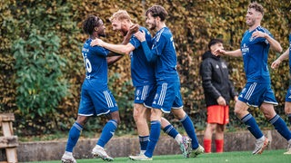 Fußballspieler des Bremer SV in dunkelblauen Trikots und Hosen bejubeln gemeinsam einen Treffer.