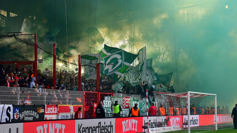 Im Werder-Fanblock im Stadion von Union Berlin brennt Pyrotechnik und die Tribüne ist grün-weißen Rauch eingehüllt.