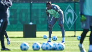 Werders Fußballprofi Skelly Alvero schaut am Rande des Trainings mit aufgestützten Armen auf die Oberschenkel zum Geschehen auf dem Platz.