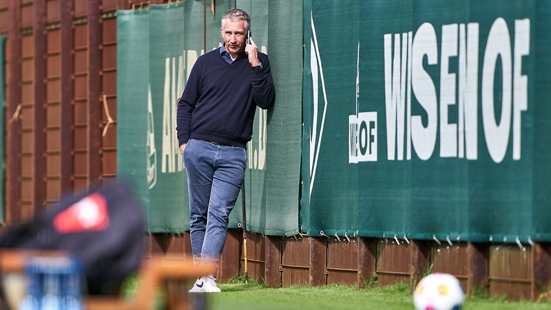 Werder-Geschäftsführer lehnt am Rande des Trainings an der Bande und telefoniert.