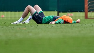 Werder-Stürmer Marvin Ducksch liegt rücklings auf dem Rasen des Trainingsplatzes und hat sich sein Leibchen übers Gesicht gezogen.