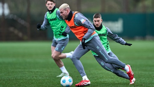 Werder-Stürmer Marvin Ducksch prescht beim Fußball-Training mit dem Ball davon, gefolgt von seinem Gegenspielern Jens Stage und Romano Schmid.