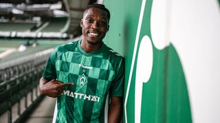 Werder-Neuzugang Derrick Köhn deutet im Werder-Trikot bei seiner Vorstellung auf die Werder-Raute darauf.