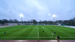 In Werders kleinem Fußball-Stadion Platz 11 brennt in der Dämmerung das Flutlicht, während sich die Werder-Profis für ein Testspiel warmlaufen.