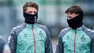 Die Werder-Profis Jens Stage und Olivier Deman haben auf dem Weg zum Trainingsplatz ihre schwarzen Loop-Schals über das halbe Gesicht gezogen.