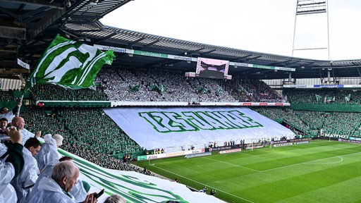 Blick auf die Westkurve des Bremer Weserstadions, wo die Fans eine große weiße Blockfahne ausgerollt haben. Auf dieser steht: "125 Jahre".