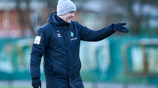 Werder-Trainer Ole Werner trägt eine graue Wollmütze rief ins Gesicht gezogen und gibt gestikulierend Anweisungen während des Trainings.