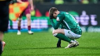 Werder-Profi Mitchell Weiser hockt nach der Heimspielniederlage gegen Augsburg frustriert auf dem Rasen und hält sich den Kopf.