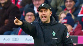 Werders Fußball-Trainer Ole Werner steht im Spiel an der Seitenlinie, gestikuliert mit ausgetrecktem, rechten Arm und ruft seinen Spielern etwas zu.