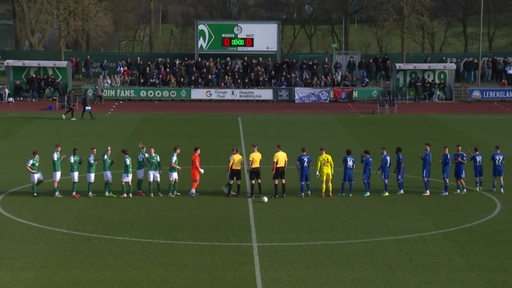 Zwei Mannschaften stehen sich vor dem Anpfiff eines Fußballspiels im Mittelkreis gegenüber.