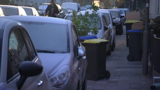 Autos in einer Straße parken verbotenerweise halb auf dem Gehweg. 