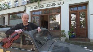 Der Geigenbauer Frank Wichmann mit Geige in einem Oldtimer vor seinem Geschäft.