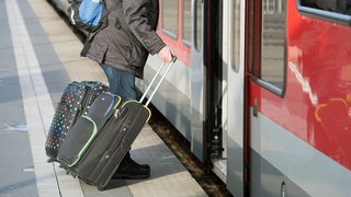 Ein Mann hat zwei Rollkoffer in der Hand und steigt in einen Zug ein