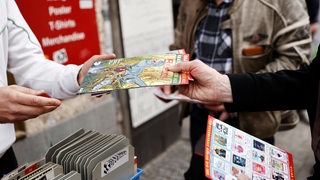 Eine Person überreicht einer anderen mehrere Comics.
