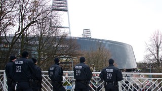 Dunkel gekleidete Polizisten stehen abwartend am Rande des Weser-Stadions.