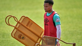 Werder-Verteidiger Felix Agu trägt nach dem Training die orangefarbenen Metallmännchen vom Platz und schaut dabei ernst.