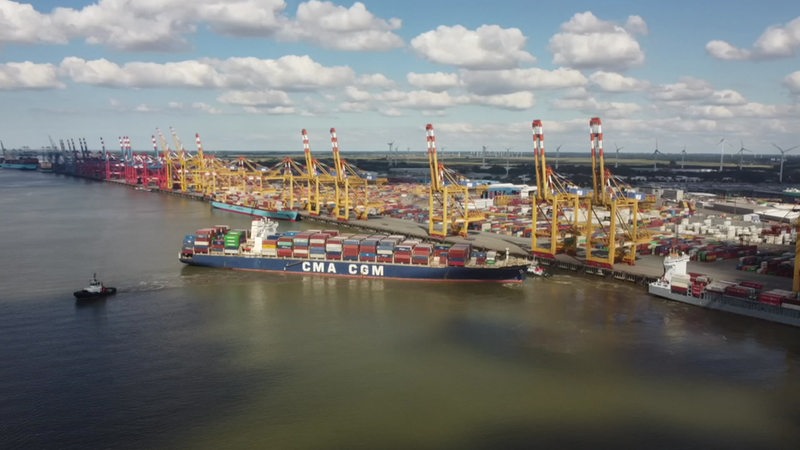 Ein Containerschiff steht vor einem Hafen mit vielen Kränen.