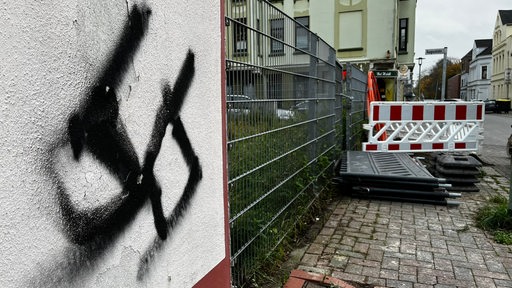 An einer Hauswand an einer Straße ist ein gesprühtes Hakenkreuz zu sehen.