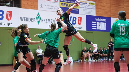 Eine Handball-Spielerin des VfL Oldenburg steht beim Wurf hoch in der Luft, die Werder-Spielerinnen können den Angriff nicht abwehren.