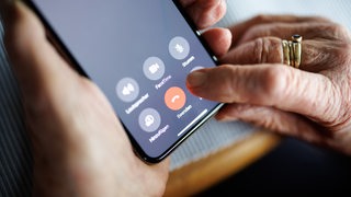 Zwei Hände einer älteren Person halten ein Smartphone. 