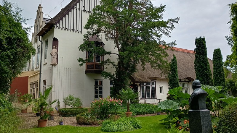 Vor einer alten Villa liegt ein Garten mit einer Statue.