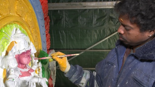 Eine Person bemalt hinduistisch aussehende Figuren bunt an.