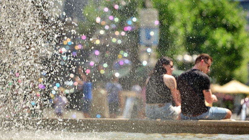 Menschen sitzen an einem Brunnen, die Sonne scheint