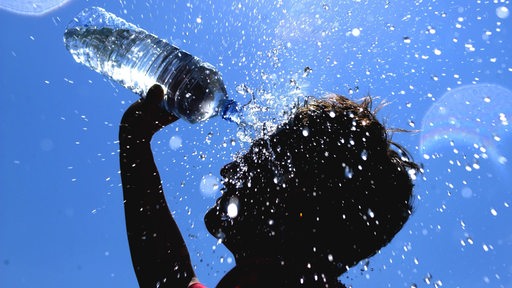 Bei strahlend blauem Himmel und tropischen Temperaturen schüttet sich ein Junge Wasser aus einer Flasche über seinen Kopf.