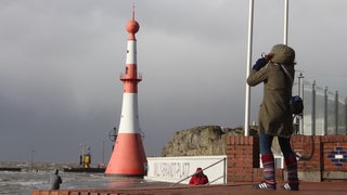 Eine Frau stemmt sich am Wasser gegen den Wind.