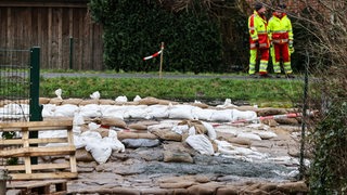 Helfer stehen hinter einem durchweichten Deichabschnitt an der Wörpe. 