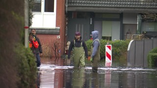 Anwohner stehen knietief im Wasser vor einem Wohnhaus.