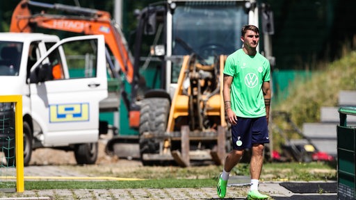 Maximilian Philipp geht im Wolfsburg-Dress in Richtung Trainingsplatz. Hinter ihm sind Baustellenfahrzeuge zu sehen.