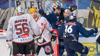 Spieler des EHC München jubeln im Hintergrund, während die Pinguins bedröppelt sind.