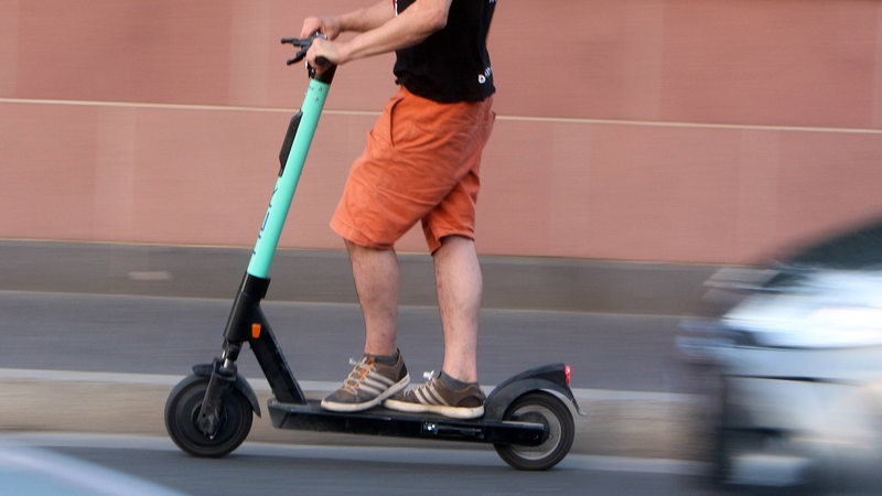 Mann fährt auf einem E-Roller und wird von einem Auto überholt.