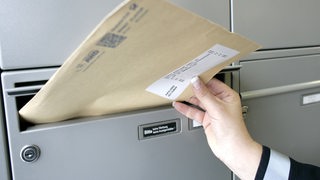 Postbotin steckt einen Brief in einen Briefkasten.