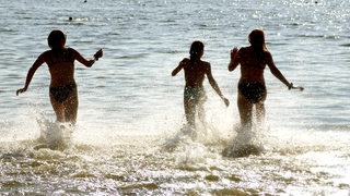 Drei Menschen laufen in einen Badesee.