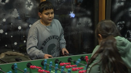 Zwei Kinder spielen Kicker gegeneinander.