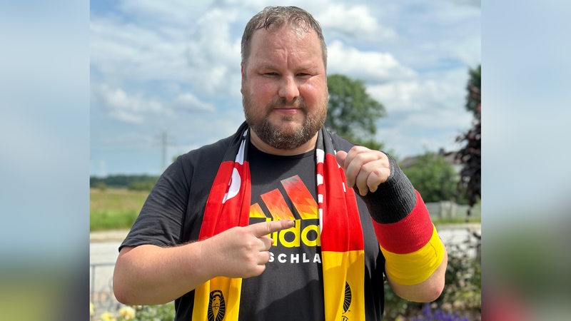 Kai Flathmann mit EM-Fanschal und einem schwarz-rot-golden Verband, auf den er zeigt