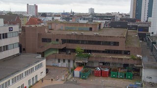 Blick auf ein braunes Gebäude. Davor stehen Container.