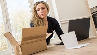 Eine Frau sitzt  vor einem Laptop und bezahlt eine Rechnung für eine Lieferung (Symbolbild)