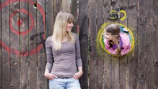 Eine junge Frau schaut ein Mädchen auf einem Spielplatz an.