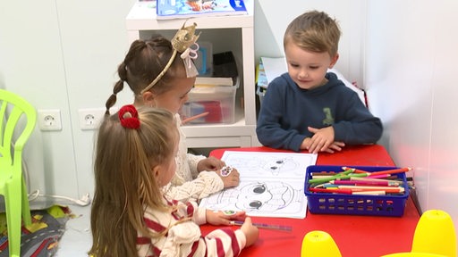 Drei kleine Kinder sitzen an einem Tisch und malen.