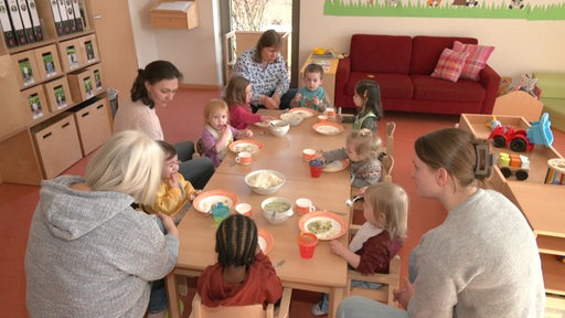 Die Kinder und Erzieherinnen der KiTa gemeinsam an einem Tisch beim Mittagessen.