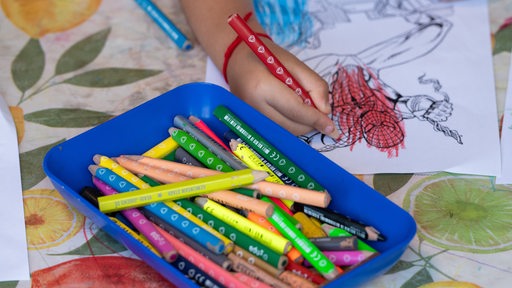 Eine Kinderhand malt mit Buntstiften eine Spiderman-Vorlage aus