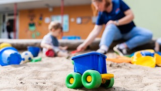 Ein Kind spielt mit einer Erzieherin im Sandkasten einer Kita.